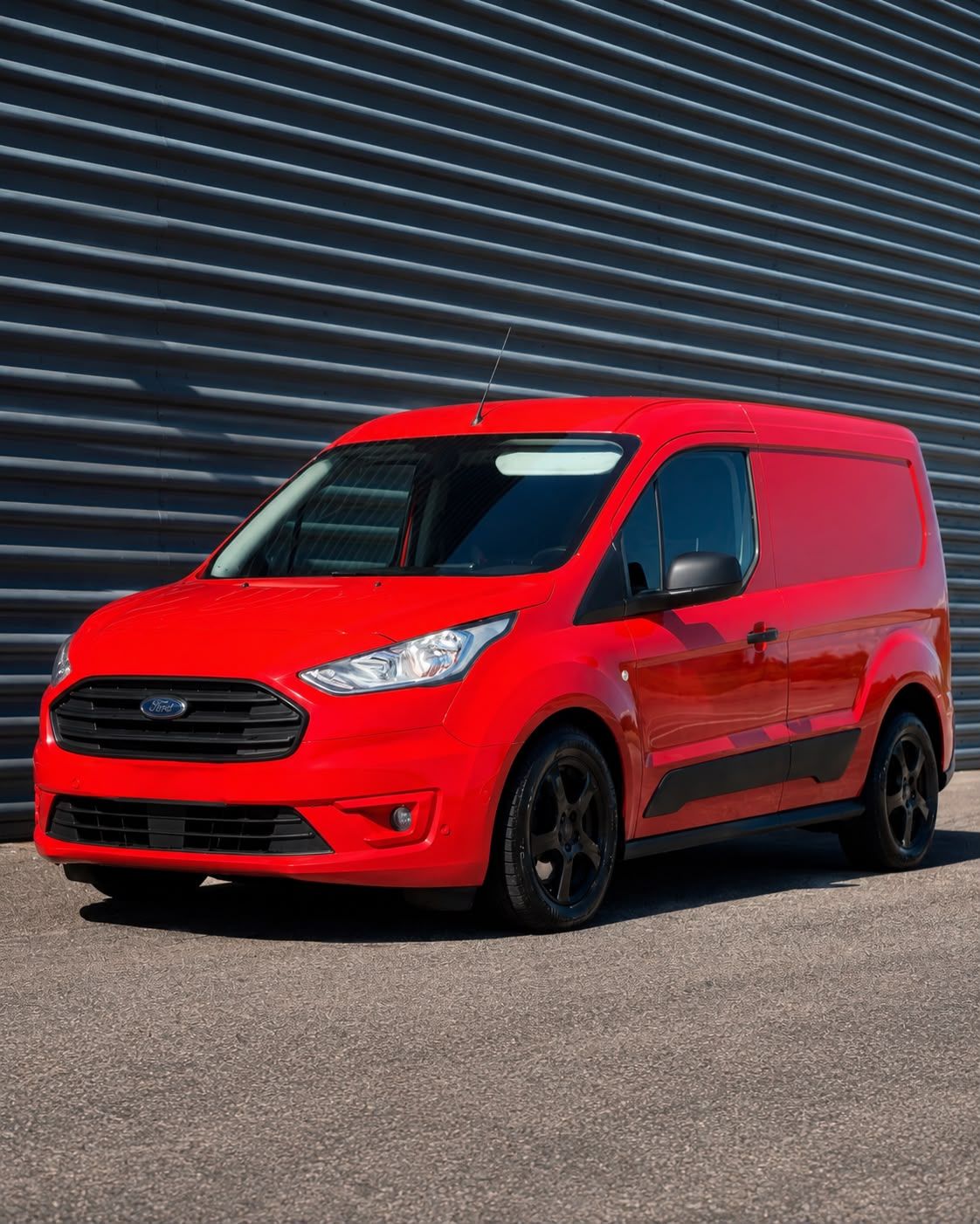 Röd Ford Transit Connect skåpbil fotograferad mot en grå korrugerad plåtvägg